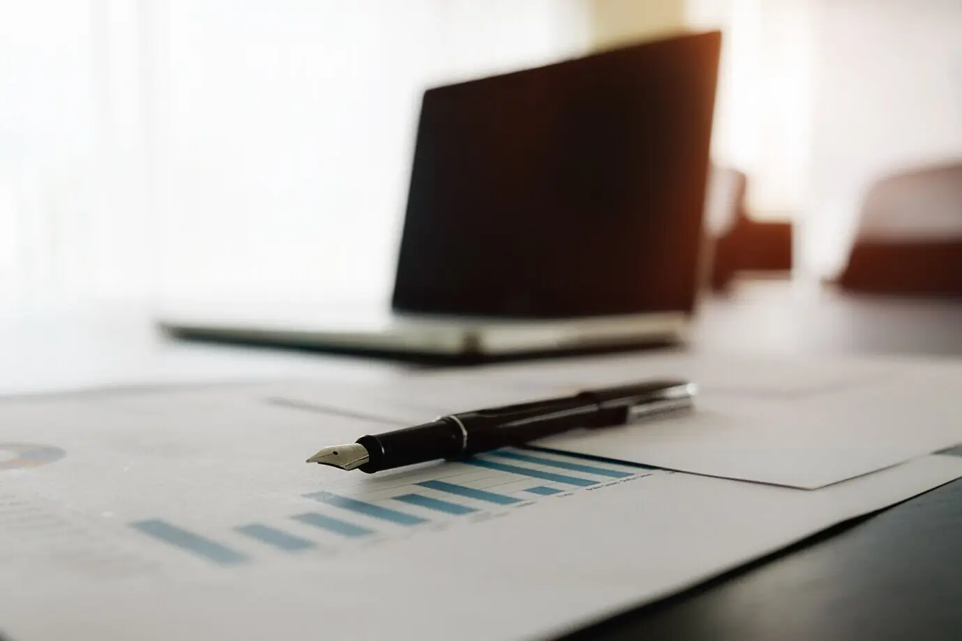 Geschäftskonzept mit freiem Textbereich: Büroschreibtisch mit Fokus auf einem Stift und einer Analysegrafik, Computer, Notizbuch und Kaffeetasse auf dem Tisch. Vintage-Ton, Retro-Filter, selektive Fokussierung.